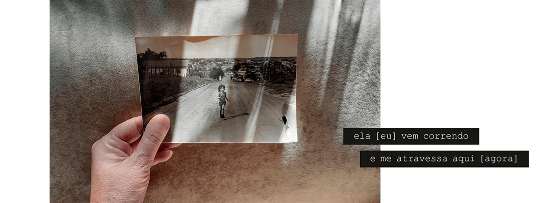 Foto horizontal com fundo bege escuro, iluminado por largas faixas verticais de luz que vem de cima. No canto de baixo, à esquerda, há uma mão segurando uma grande foto antiga em preto e branco. Esta foto mostra uma criança de quatro anos correndo em direção à câmera, sorrindo, numa longa estrada de terra que desce em perspectiva. Ao longe há uma cidadezinha do interior. As faixas de luz da foto maior também estão sobre a foto antiga. Há uma frase em duas faixas pretas que começam no lado direito e saem da margem: ela [eu] vem correndo e me atravessa aqui [ agora ]. (Esta é a última imagem da série.)