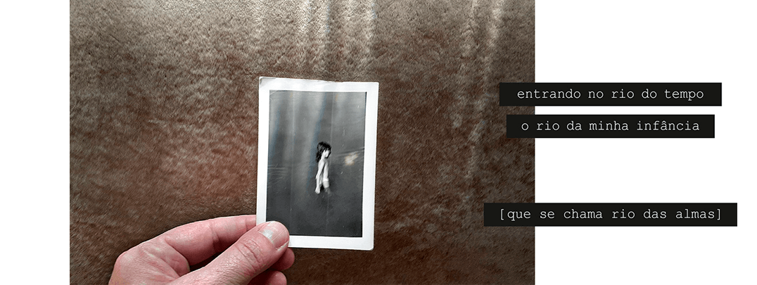 Foto horizontal mostrando parte de uma mão segurando uma foto pequena contra um fundo bege, com sombras e luzes que vêm de cima. A foto pequena está no centro. Pequenas faixas verticais de luz que iluminam o fundo bege iluminam também a foto pequena, que é antiga e em preto e branco. Ela mostra uma menina entrando na água de um rio ou lago, em meio perfil, com água até a parte de cima das coxas. A menina está longe e parece ter se virado para olhar para a câmera. Há uma frase em três faixas pretas que começam no lado direito e saem da margem da foto: entrando no rio do tempo / o rio da minha infância / [que se chama rio das almas].