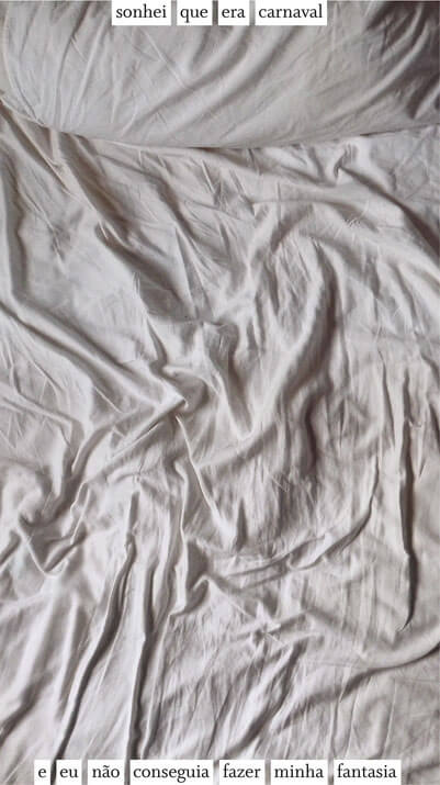 Foto vertical colorida mostrando apenas um lençol branco amarrotado e metade de um travesseiro branco. Há uma frase escrita em preto sobre uma estreita faixa branca. Parte da frase está colada à margem de cima, centralizada, e parte colada à margem de baixo: sonhei que era carnaval / e eu não conseguia fazer minha fantasia.
