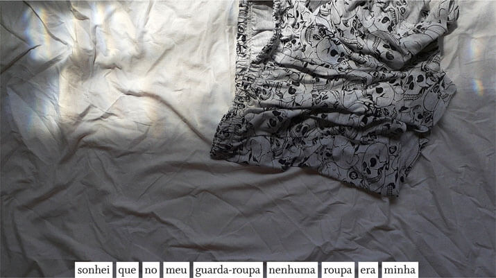 Foto horizontal colorida de um short de pijama branco, com estampa de caveiras em preto, sobre um lençol branco e amarrotado. A roupa está na parte de cima, onde há uma faixa de luz do sol. Na parte de baixo, colada à margem, há uma frase sobre uma estreita faixa branca: sonhei que no meu guarda-roupa nenhuma roupa era minha.
