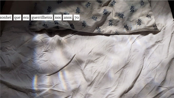 Foto horizontal colorida mostrando parte de um travesseiro e, na maior parte, um lençol amarrotado. A fronha tem pequenas flores em azul escuro sobre fundo branco, e o lençol é branco. A imagem está iluminada pela forte luz do sol. À esquerda e em cima há sombras escuras, contrastantes. Colada à margem esquerda, sobre as sombras, está uma frase numa faixa branca: sonhei que era guerrilheira nos anos 70.