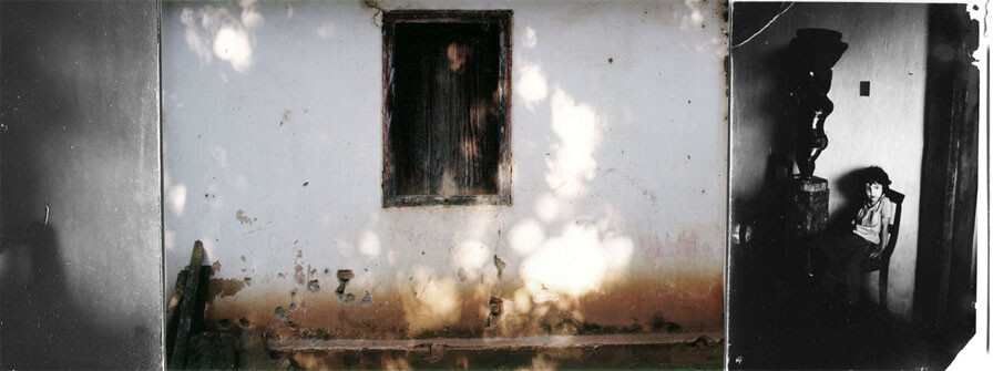 Colagem digital em formato panorâmico. No centro há uma foto horizontal colorida de uma janela fechada, simples, de madeira escura, no centro de uma parede branca com rachaduras e manchas de barro. A parede tem manchas brancas do sol filtrado pela sombra de árvores. À direita desta imagem há uma foto vertical, preto e branca, de uma criança sentada numa cadeira, olhando para o lado. Está a meia distância e tem uma expressão entre curiosa e assustada. A cadeira está encostada numa parede branca, entre o que parece ser uma grande porta de madeira escura e um pedestral com uma grande peça de madeira trabalhada. Não é possível distinguir os detalhes pois a foto é muito escura, exceto pela luz lateral que bate na criança e na parede. Suas bordas são irregulares e desgastadas. Na parte esquerda da colagem há uma estreita faixa vertical com o detalhe de uma sombra na parede preta e branca.